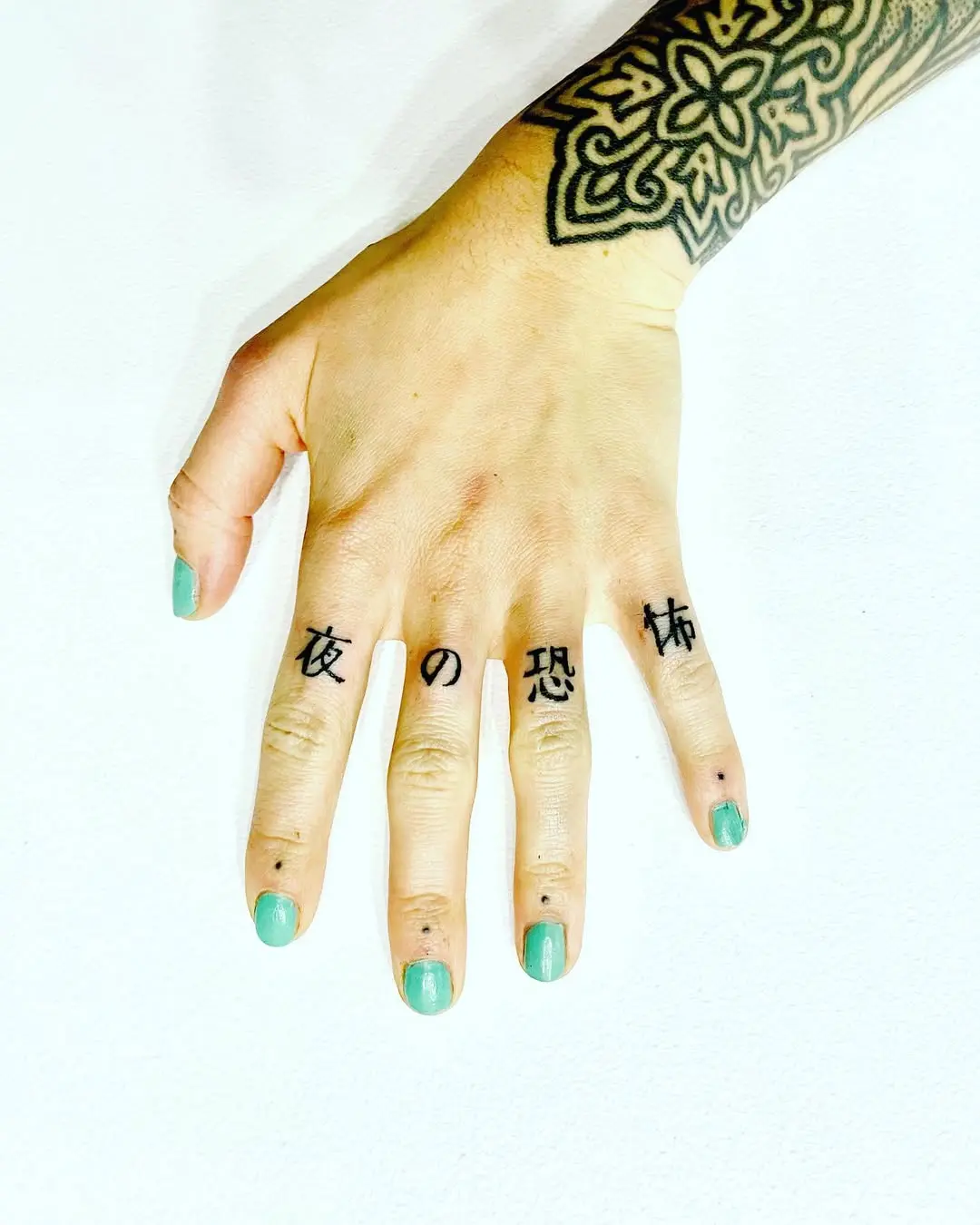 Photo d'une main tatouée avec la technique du handpoke. Le tatouage réprésente des idéogrammes japonais