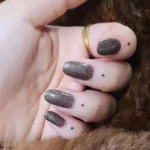 Photo de doigts tatoués au handpoke avec des petits points noirs.