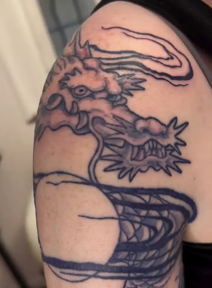 Photo d'un tatouage de dragon bleu entouré de nuages sur un bras